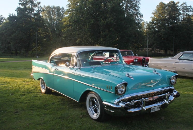 A beautiful teal and white classic car with chrome detail next to other classes cars