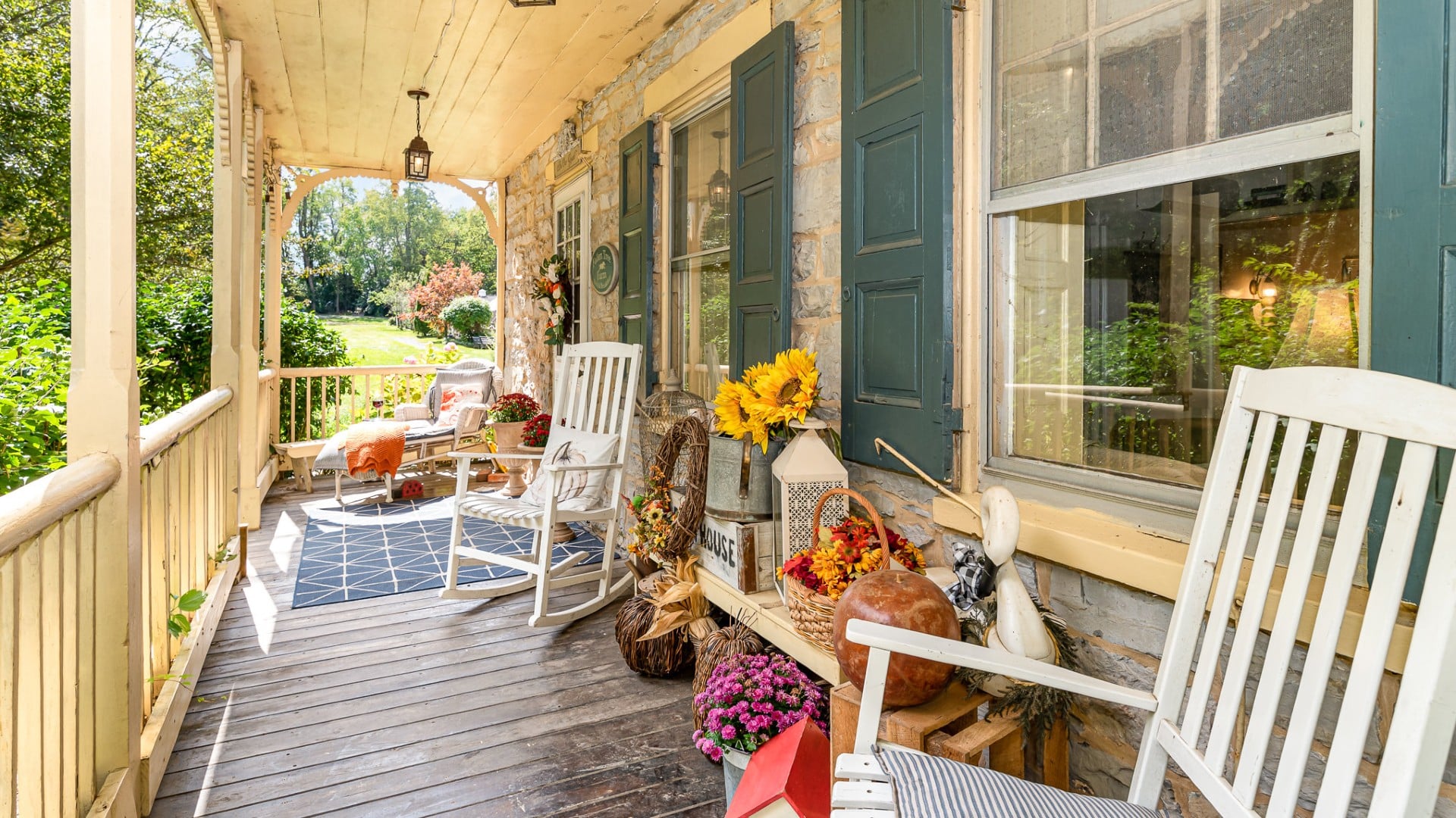 Outdoor porch of a home with decor for fall with two white rocking chairs and chaise lounge