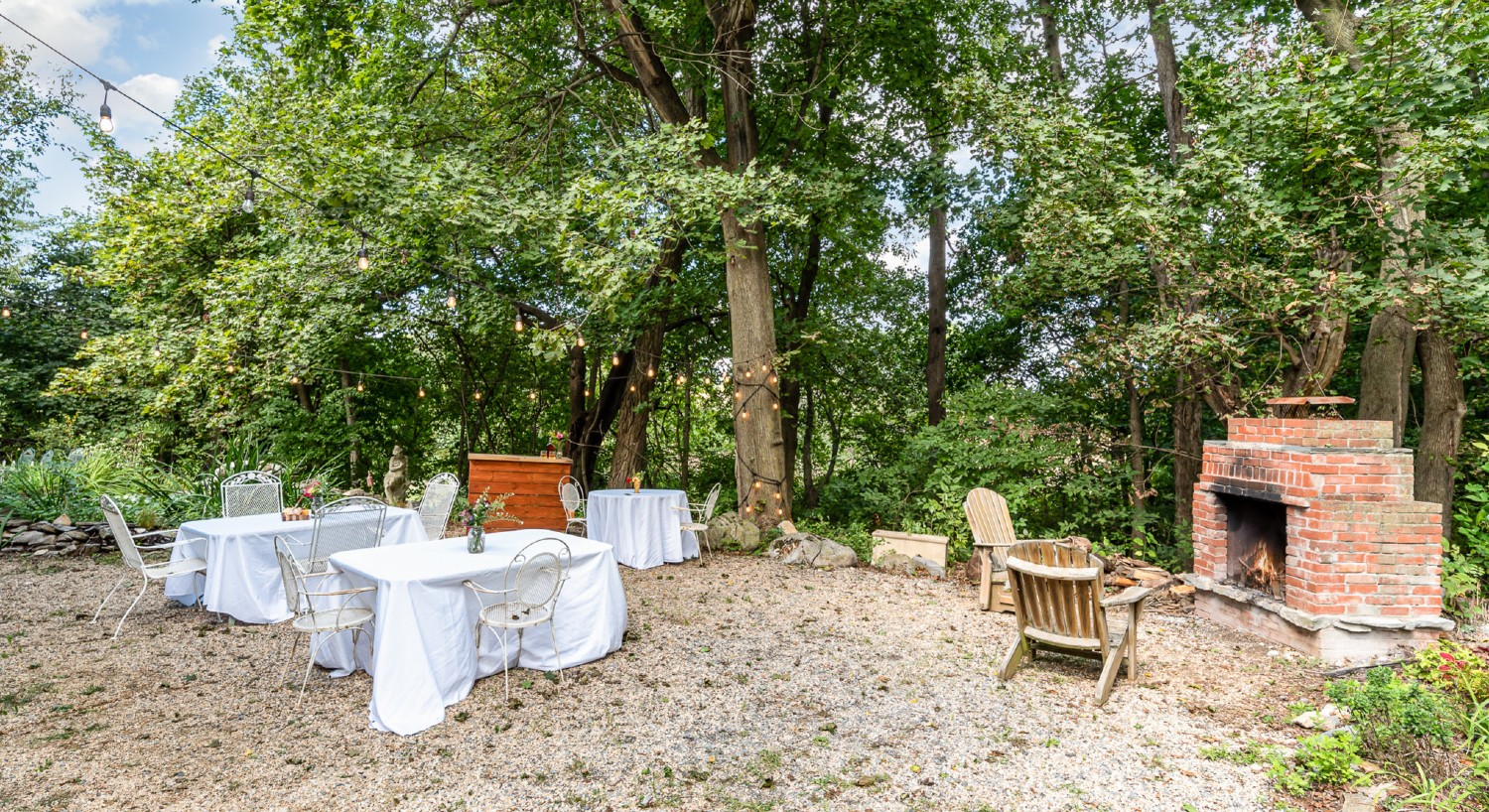 Outdoor firepit area with two adirondack chairs and tables with white cloth and patio chairs