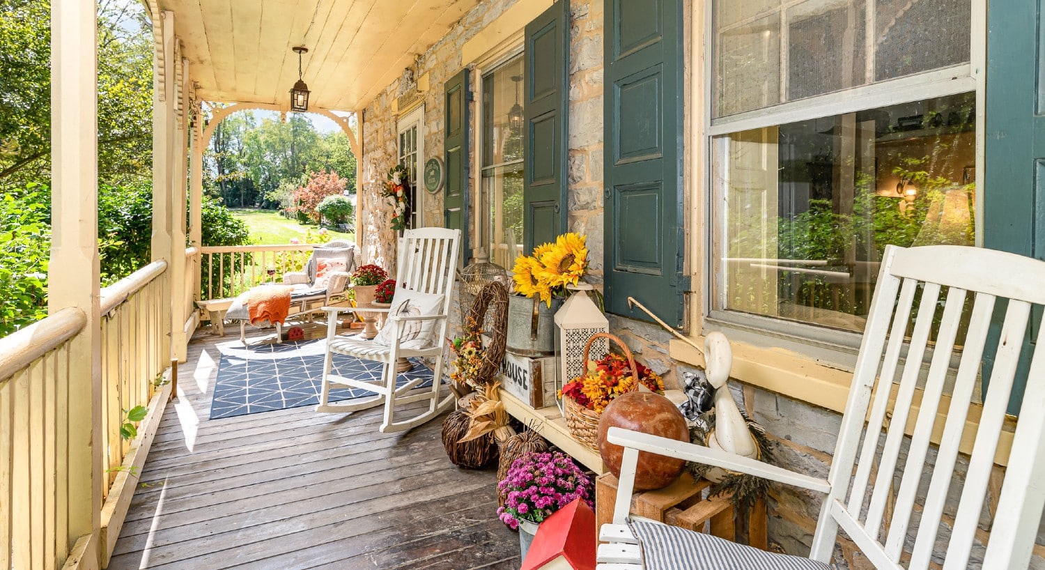 Outdoor porch of a home with decor for fall with two white rocking chairs and chaise lounge