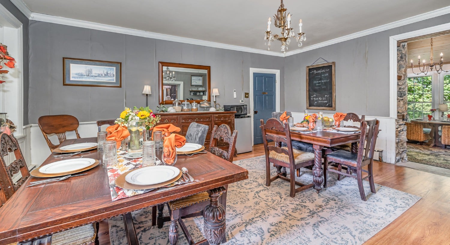 Gorgeous dining area of a home in hues of grey with two tables set for breakfast and doorway into an adjacent room
