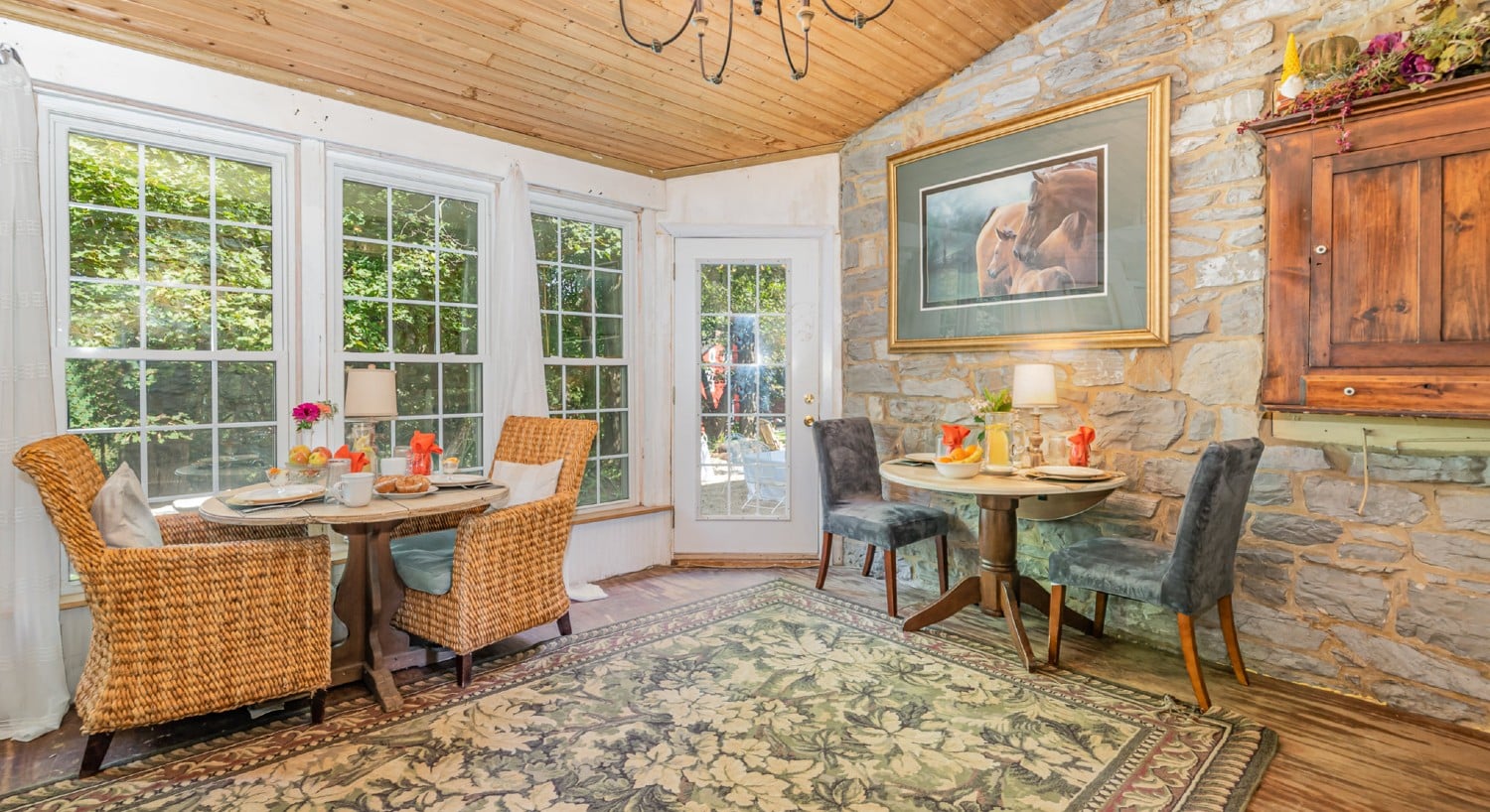 Cozy breakfast nook with two tables for two by a stone wall and wall of windows on the other side