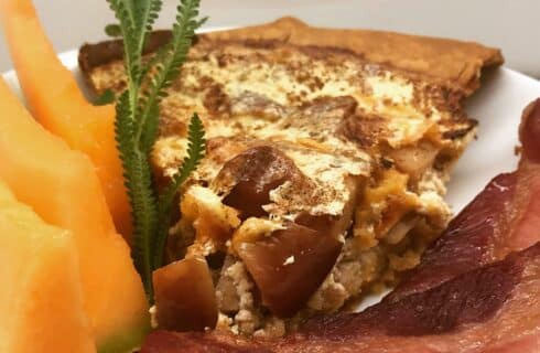 Delicious slice of quiche with cantaloupe slices and bacon
