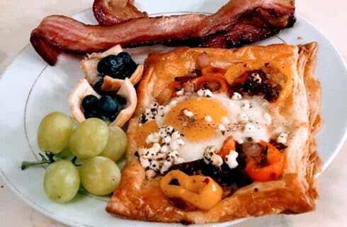 Delicious breakfast plate of an egg puff pastry, grapes, bacon and blueberries