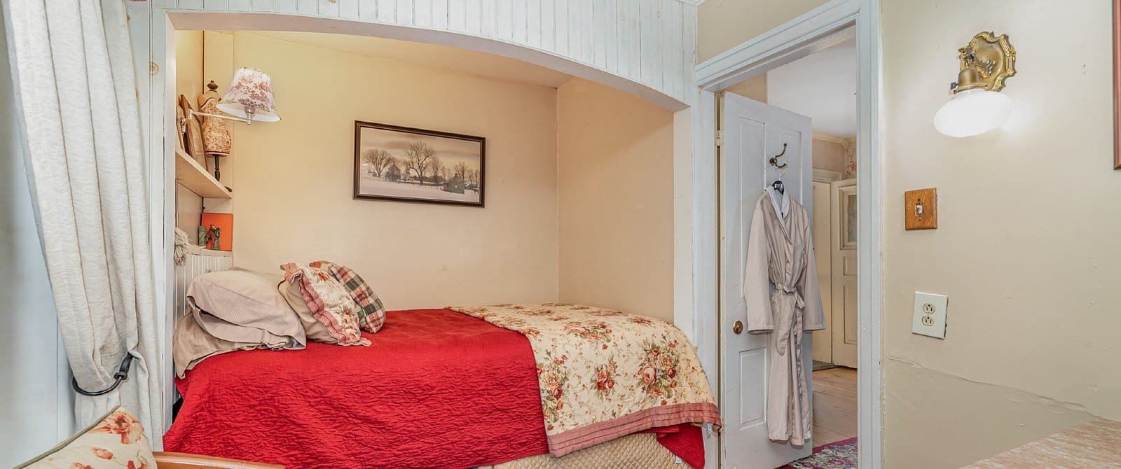 Bedroom with queen bed in a small nook with doorway open to a bathroom with a robe hanging on a hook