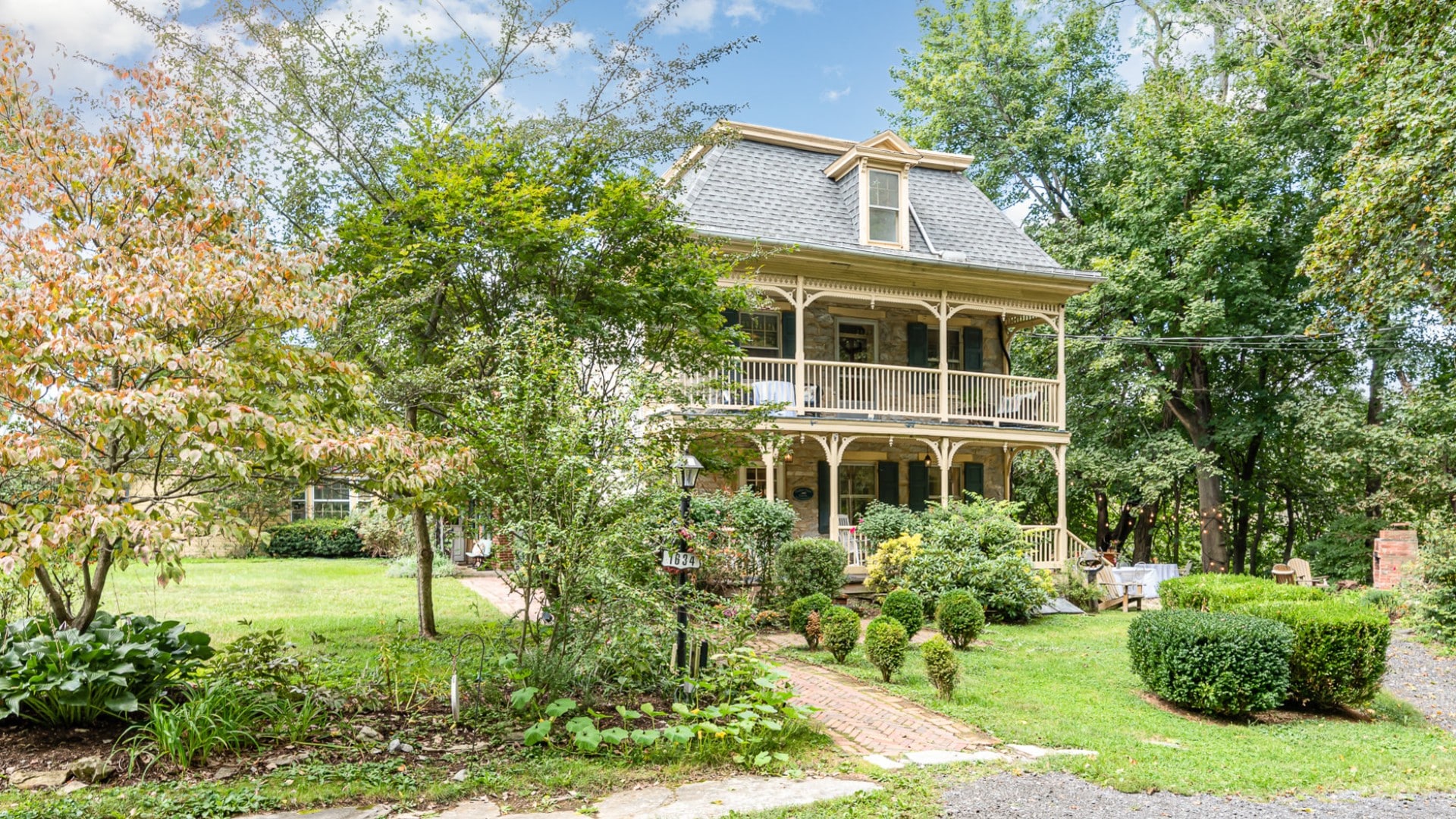 Front facade of a stately two story home with large outdoor porches, trees and lush landscaping