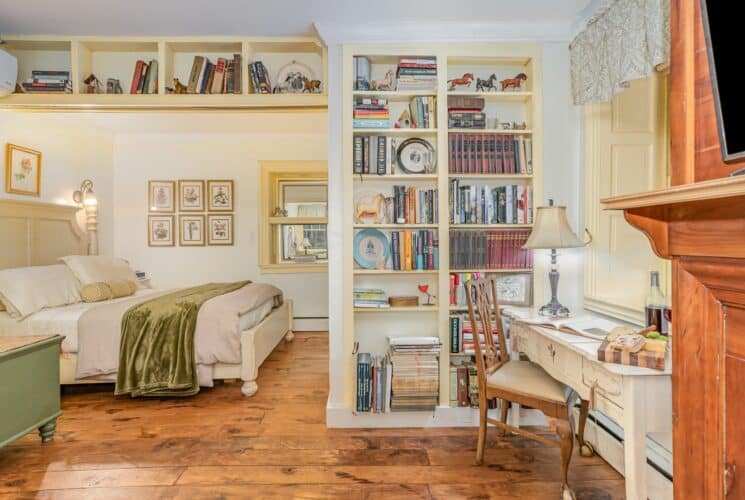 Spacious bedroom with bed in a nook, built-ins full of books, writing desk and fireplace
