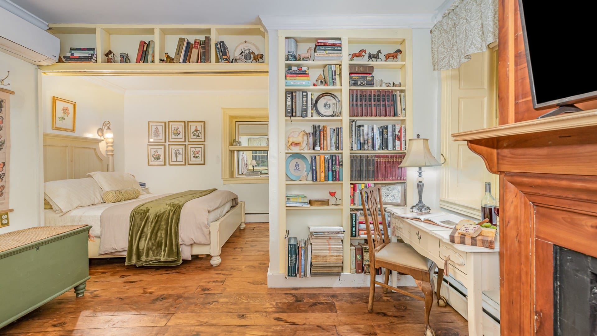 Spacious bedroom with bed in a nook, built-ins full of books, writing desk and fireplace