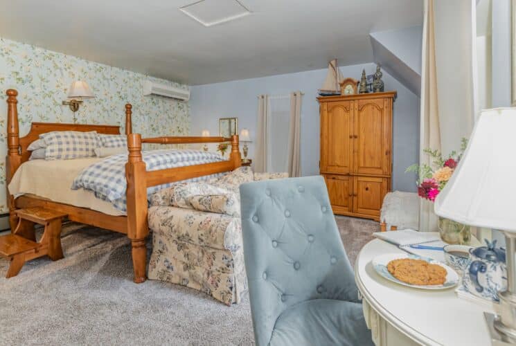 Cozy and elegant bedroom in blue hues with wood bed, floral couch, armoire and desk with sitting chair