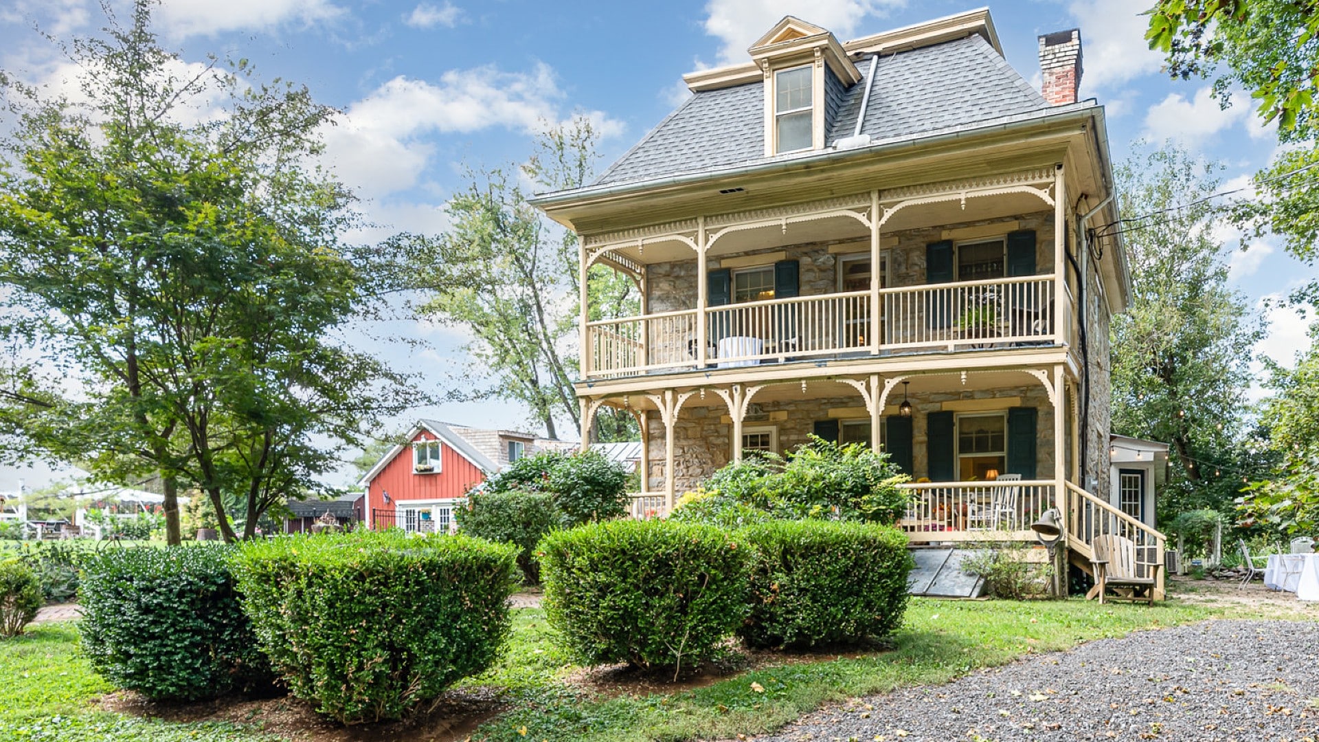 The front facade of a stately two-story home with upper and lower porches, surrounded by trees and bushes.