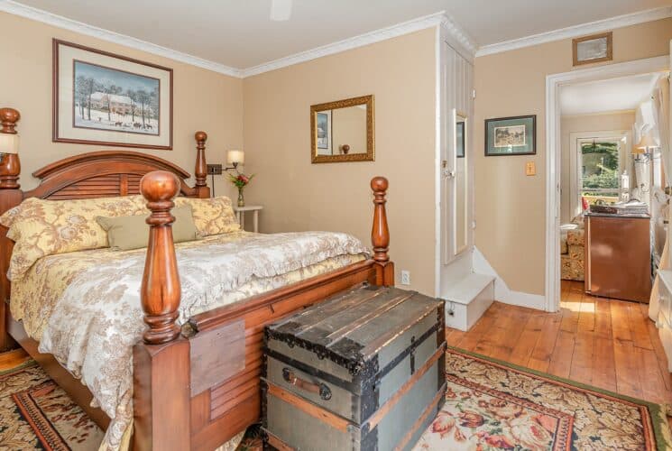 Bedroom with four poster bed, hardwood floors, decorative rug and doorway leading to an adjacent living room
