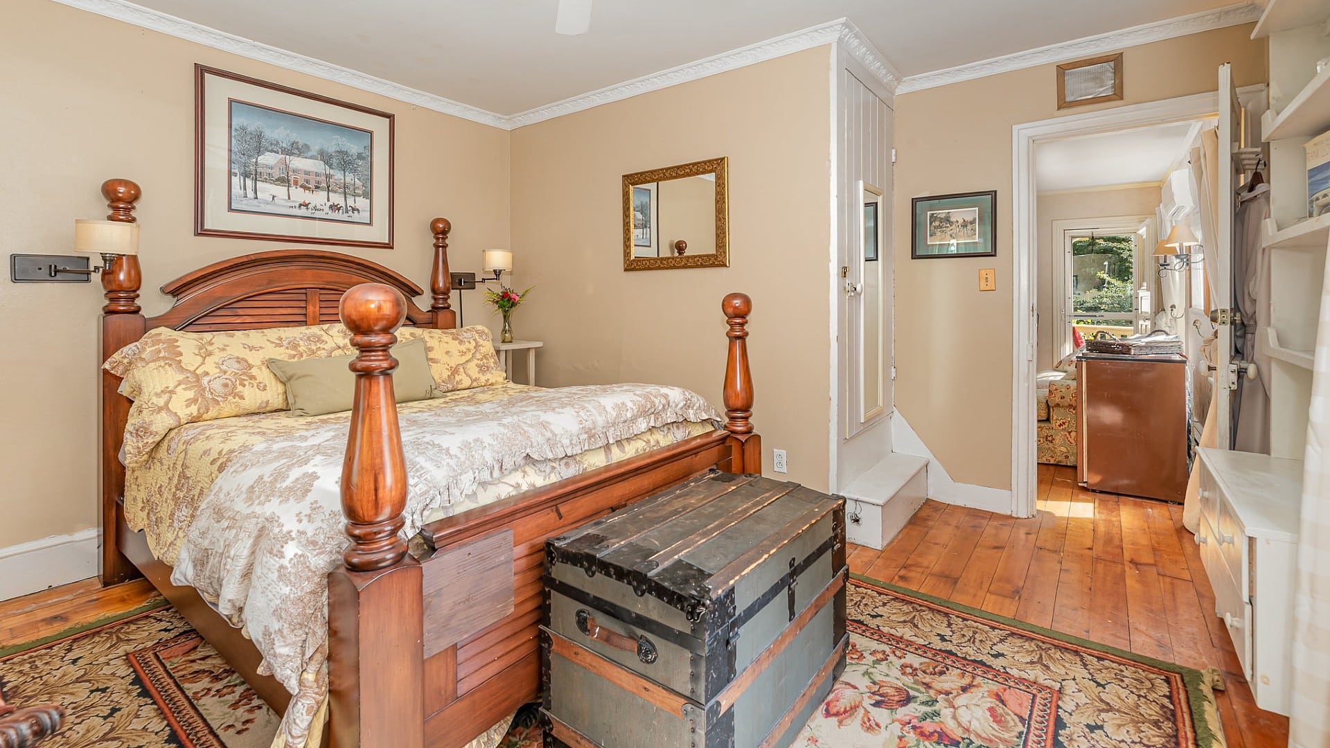Bedroom with four poster bed, hardwood floors, decorative rug and doorway leading to an adjacent living room