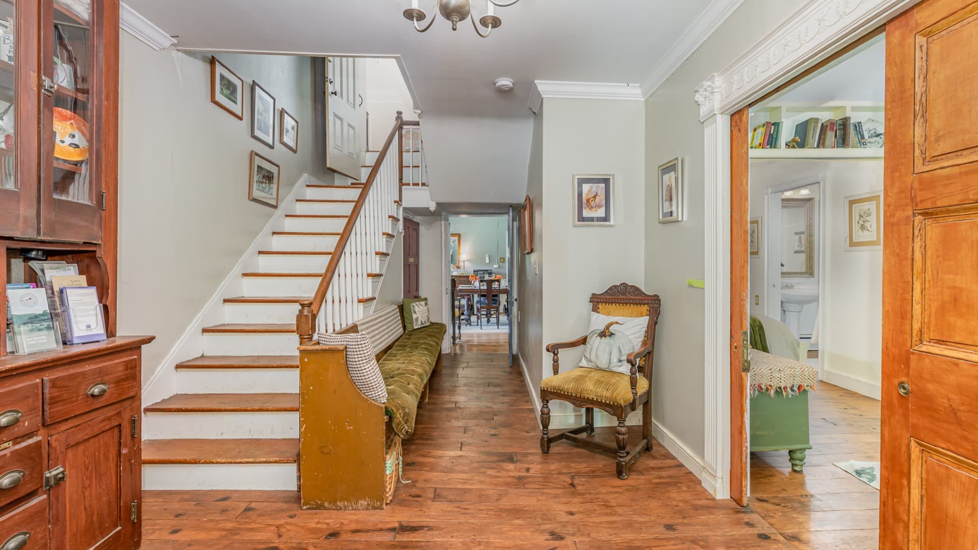 Front foyer of a home with staircase leading upstairs, a hallway and pocket doors open to an adjacent room