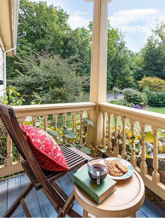 Brown chair with red pillow and table with cookies, tea and a book on the corner of an outdoor deck
