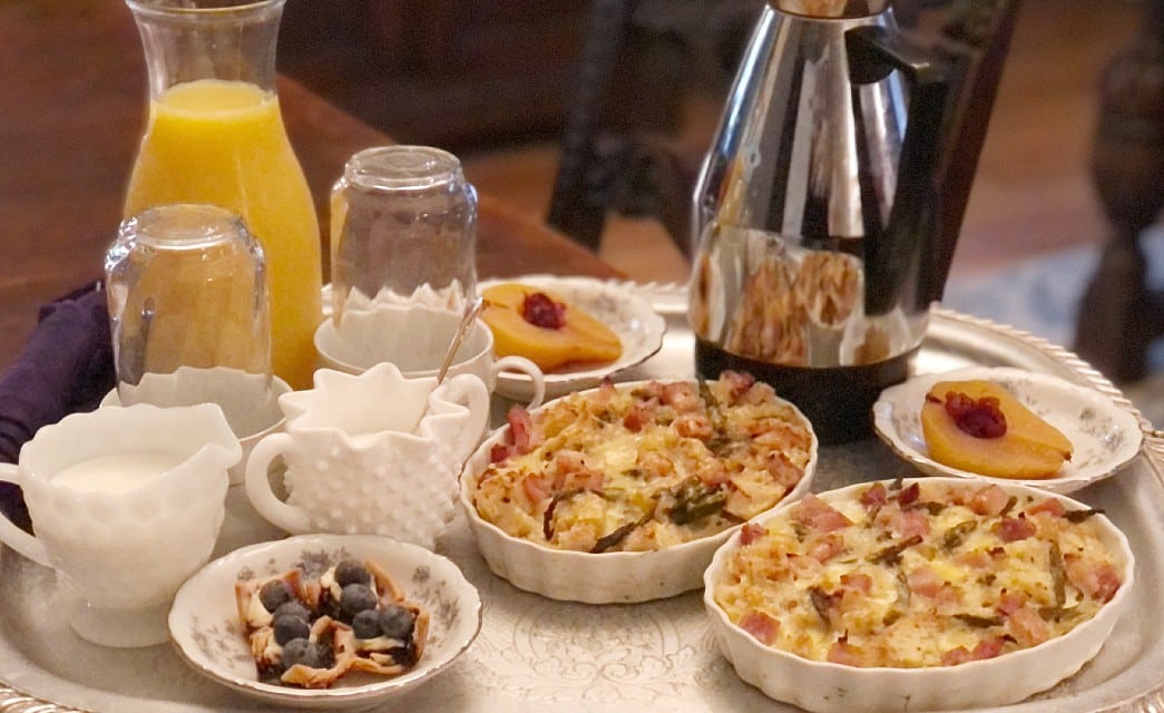 Breakfast for two with egg dishes, fruit, orange juice and coffee on a round silver platter