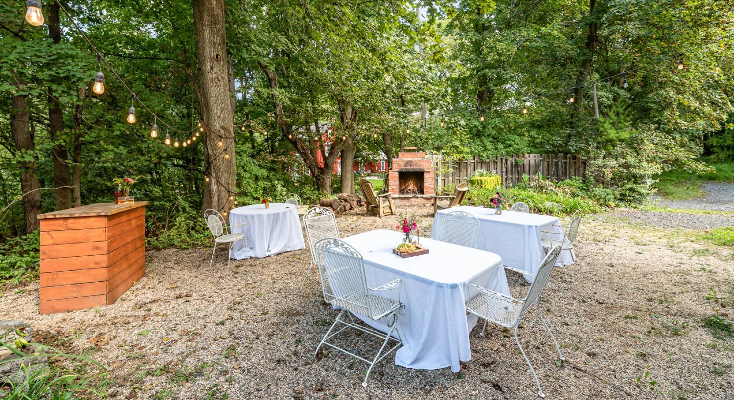 Outdoor firepit and bar area with two adirondack chairs and tables with white cloth and patio chairs