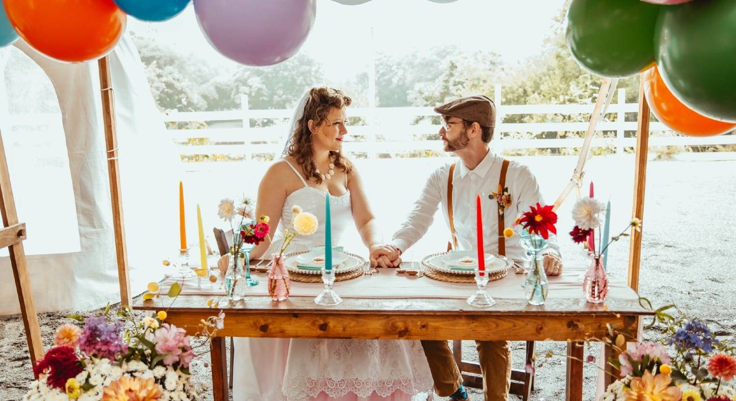 A bride and groom at a table for two surrounded by flowers and balloons