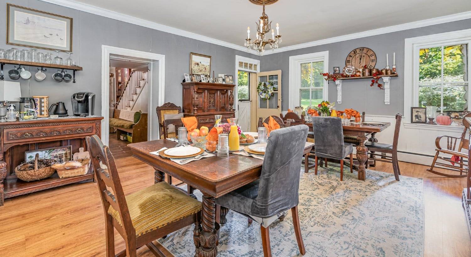 Dining room of an elegant home with two tables set for four, a coffee station and various antique pieces