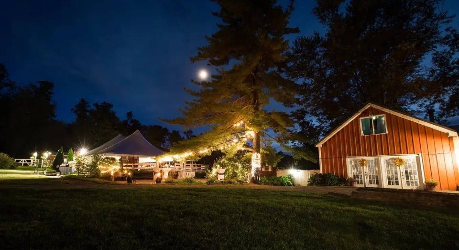 An outdoor tented reception area lit up at night with a bright moon in the sky