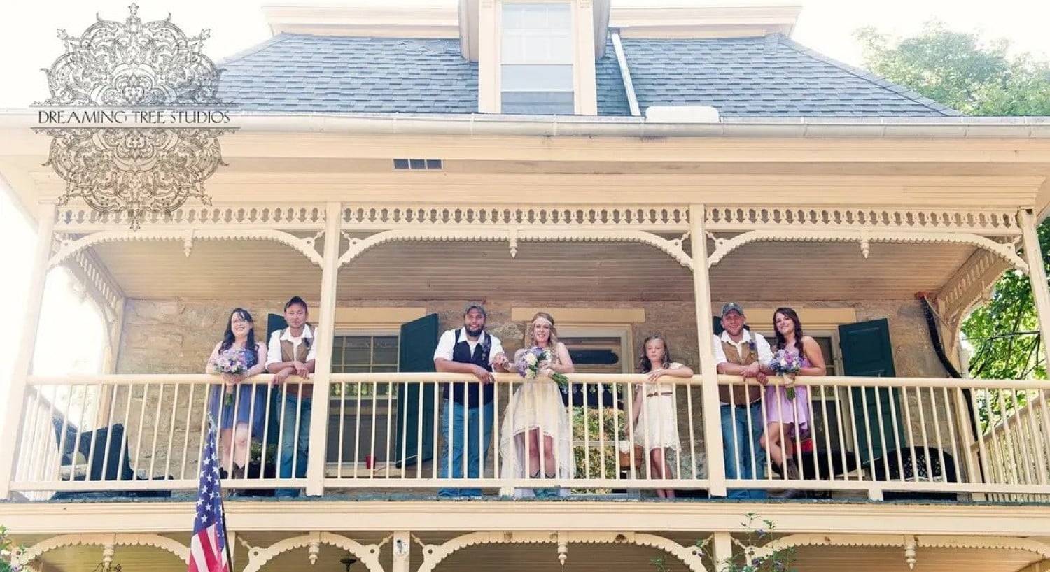 A bride and groom and their attendants standing at the railing of an upper patio of a two-story home
