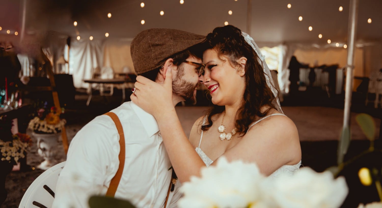 A bride and groom looking into each other's eyes in a white reception tent with string lights
