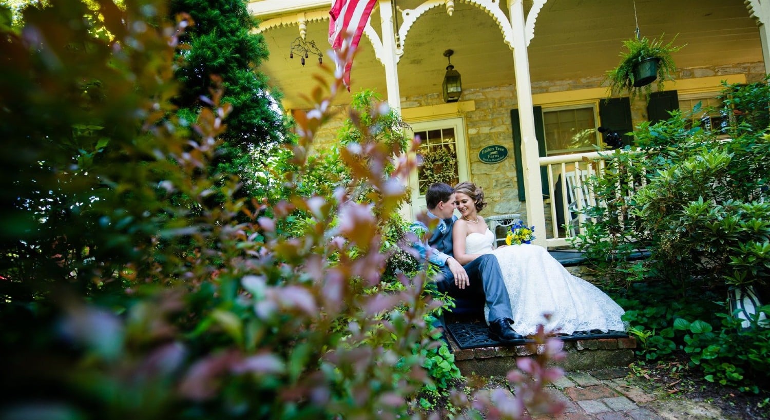 View through trees of a bride and groom sitting on a front porch of a home