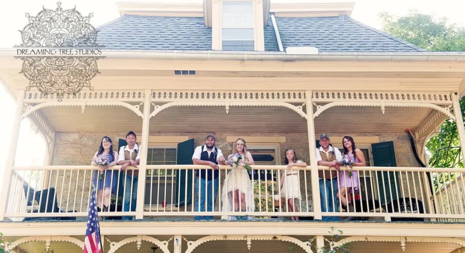 A bride and groom and their attendants standing at the railing of an upper patio of a two-story home